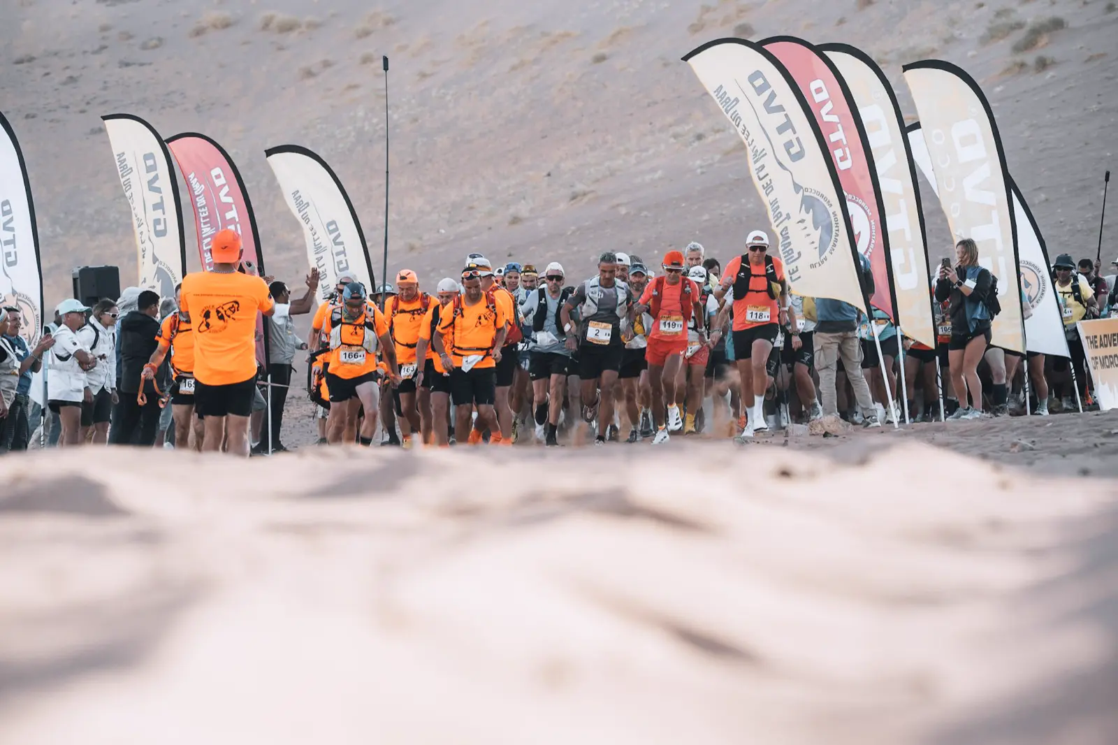 Les bénévoles en orange et les coureurs au départ d'une course dans le désert